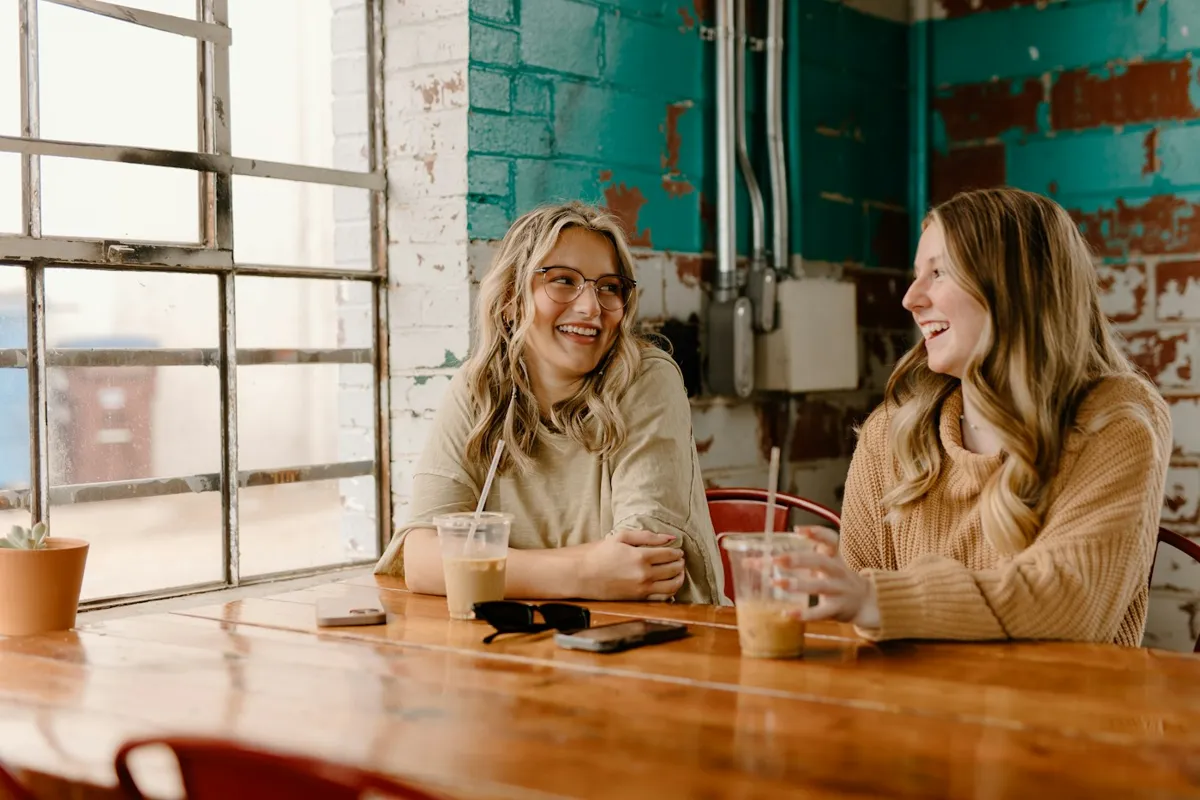Two friends laughing over coffee at a café table